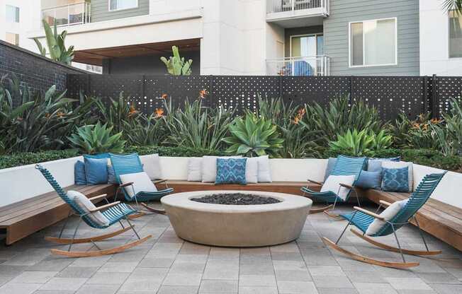 A patio with a fire pit surrounded by chairs and plants.