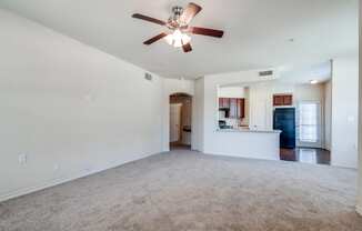 an empty living room with a ceiling fan and a kitchen