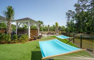 a row of hammocks in a backyard with a pool and gazebo