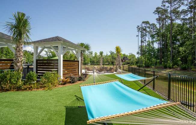 a row of hammocks in a backyard with a pool and gazebo