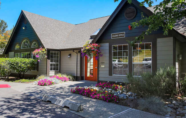 A house with a brown door and windows with flowers in front.