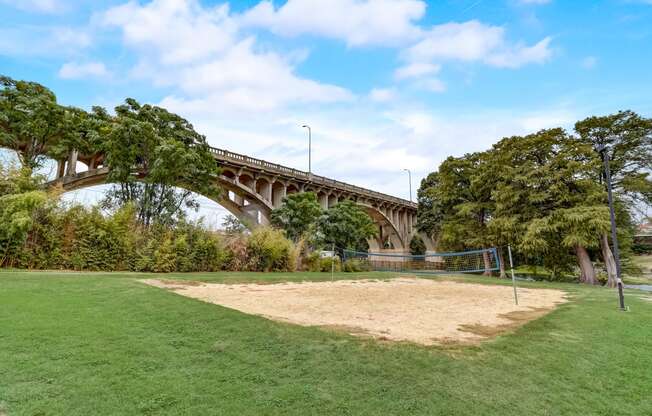 a volleyball court in a park with a bridge in the background