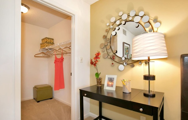 a living room with a mirror and a dresser with a lamp and a closet