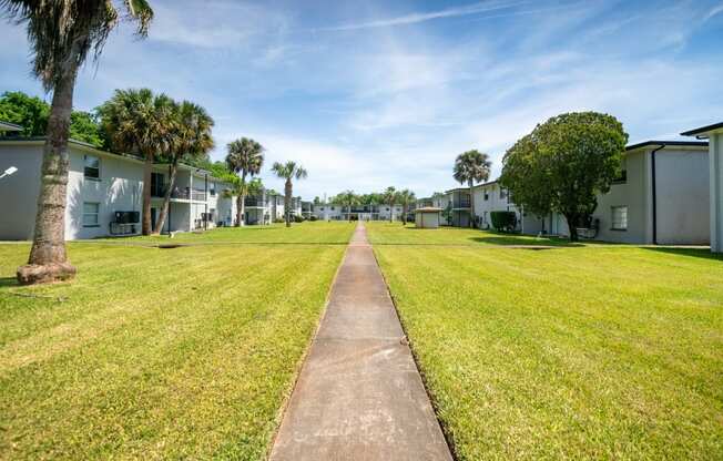 a grassy area with houses on both sides and a sidewalk