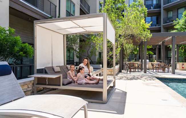 A woman and two children are sitting on a couch under a canopy on a patio.