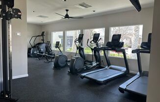 a gym with cardio equipment and windows in a buildingat Lincoln Park Apartments, Corona California