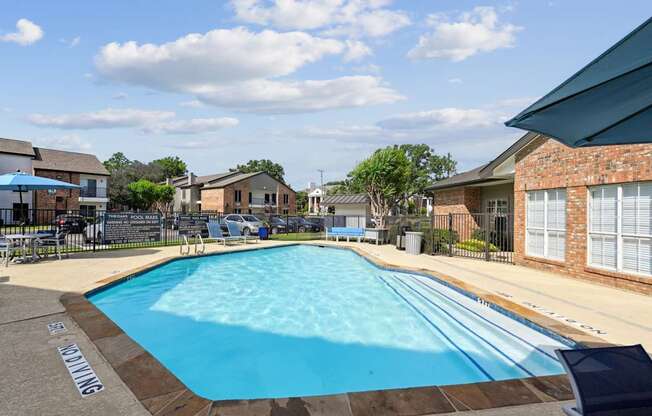 An outdoor swimming pool with apartment buildings in the background at The Oaks of Denton Apartments in Denton, TX