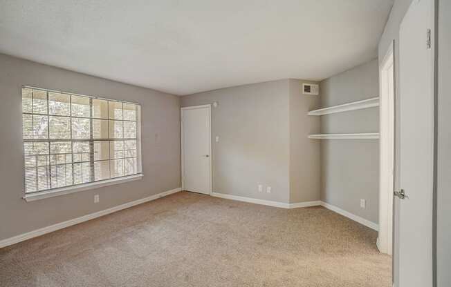 an empty bedroom with a large window and white shelves