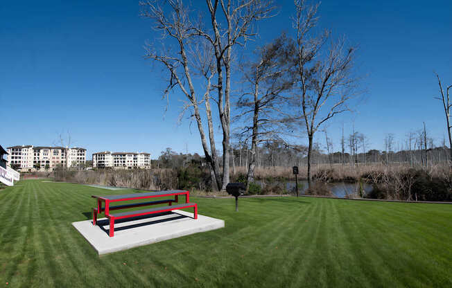A red bench sits on a concrete slab in a grassy field at Mandarin Bay Apartments.