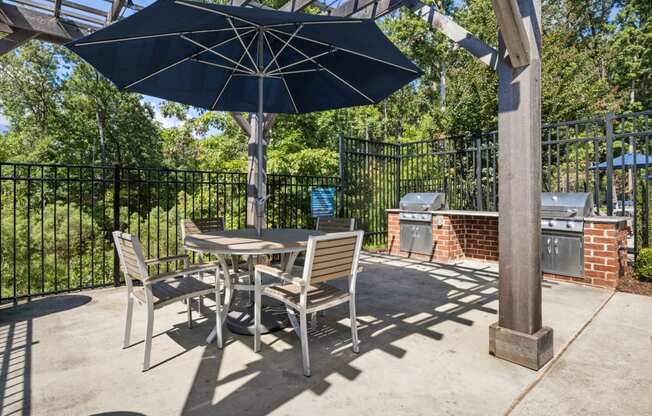 a grilling patio with a table and chairs under an umbrella
