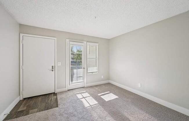Model living room with a white door, a window with blinds, and a carpeted floor.