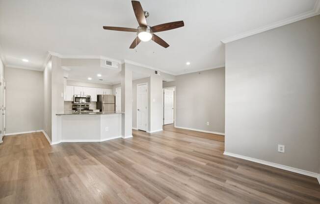 an empty living room with a ceiling fan and a kitchen