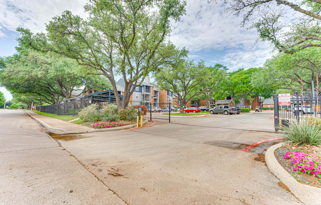 A tree-lined street with a sidewalk and a fence.