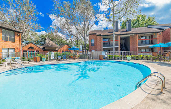 A large swimming pool in front of a building with a blue sky and clouds in the background.