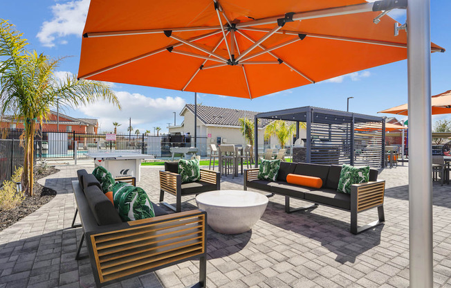 A patio with a table, chairs and an orange umbrella.