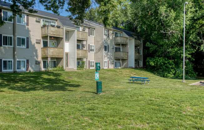 a grassy area with a picnic table in front of an apartment building