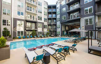 an outdoor pool with lounge chairs and tables at an apartment building