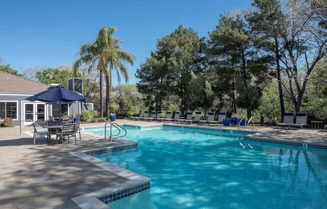 A swimming pool surrounded by trees and a patio with chairs and a table at Kirker Creek Apartments, California, 94565