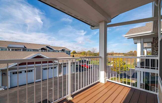 A white railing on a wooden deck with a view of a house and cars.