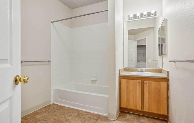 A white bathroom with a wooden cabinet and a white tub.
