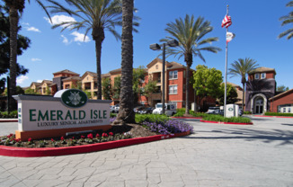 The sign for Emerald Isle Luxury Senior Apartments is in front of some palm trees.