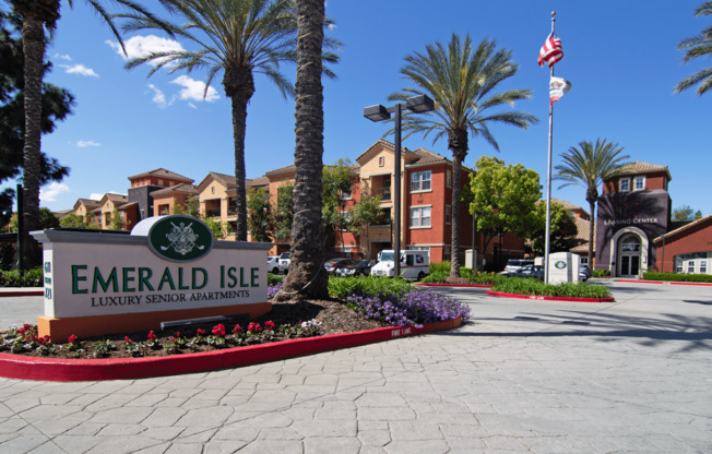 The sign for Emerald Isle Luxury Senior Apartments is in front of some palm trees.