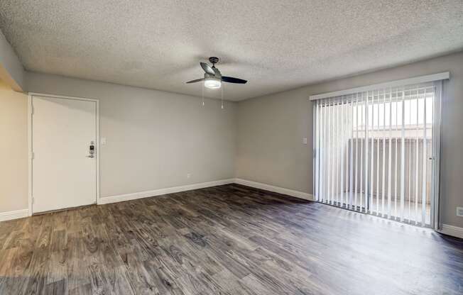 an empty living room with a large window and a ceiling fan