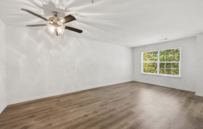 an empty living room with a ceiling fan and a window