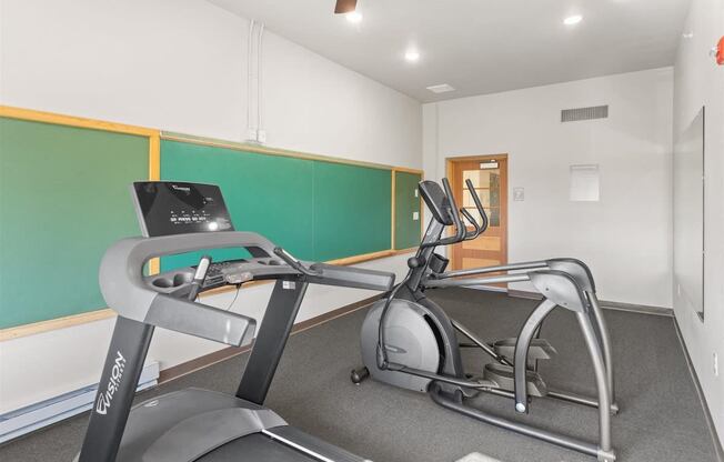 a fitness center with cardio machines, wall chalkboards and a mirror