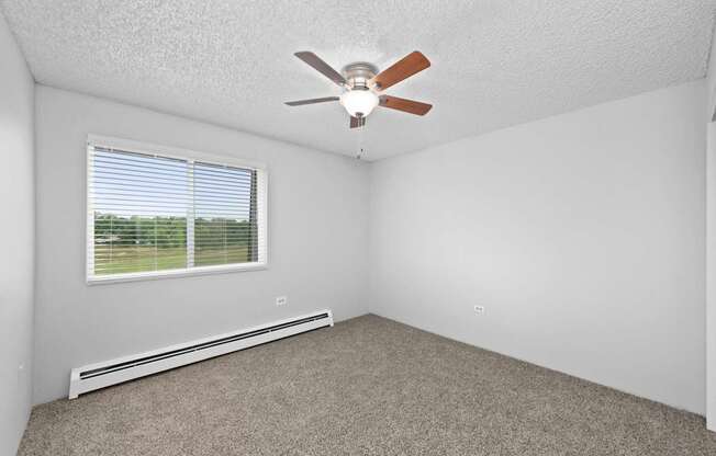 A room with a ceiling fan and a window with blinds.