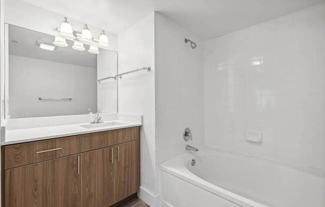 A white bathroom with a wooden vanity and a white bathtub.