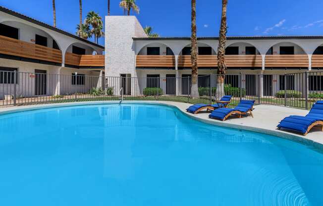 a swimming pool with blue chaise lounges and a building in the background