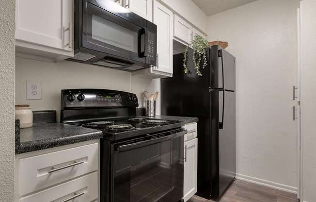 A black refrigerator stands in a kitchen with white cabinets and a black stove.