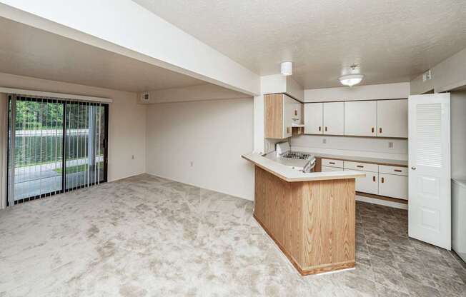 A large, empty room with a kitchenette and a sliding glass door leading to a patio.