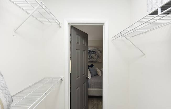 a white closet with white shelves and a door open to a room with a couch