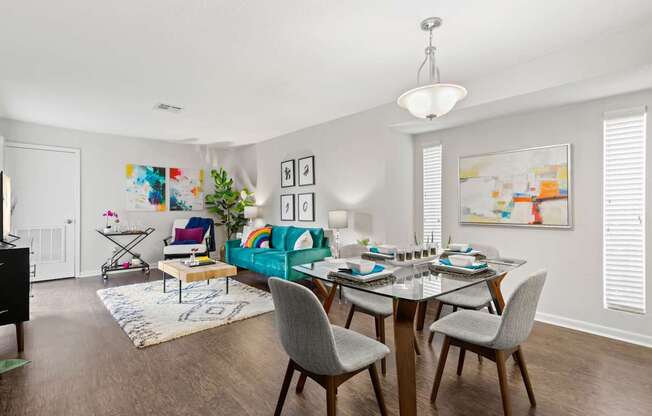 A dining room with a table set for six and a couch with a green throw pillow.