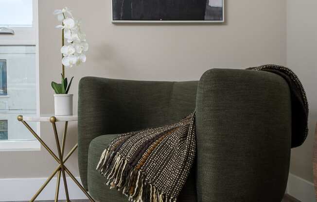 a living room with a green chair and a white orchid in a white vase