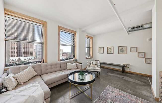 A living room with a grey sofa, a coffee table, and a large window with a view of the city.