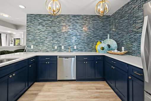 A kitchen with dark blue cabinets and a blue tiled backsplash.