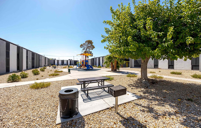 a playground with a picnic table and a tree in front of a building