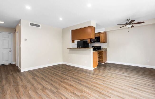 an empty living room with a kitchen in the background