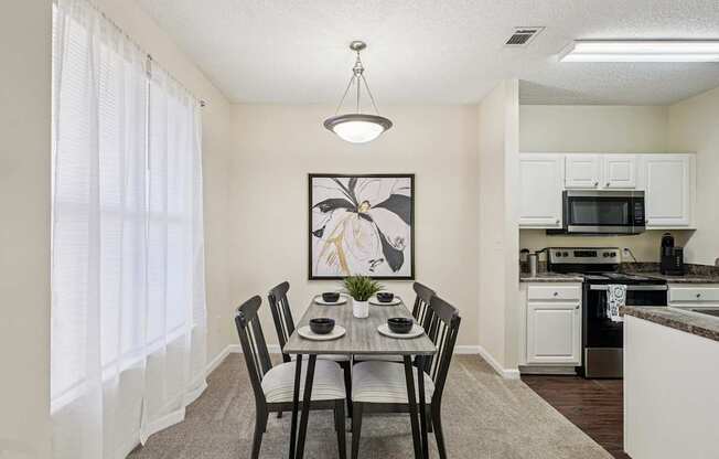 A dining room with a table set for two and a kitchen in the background.