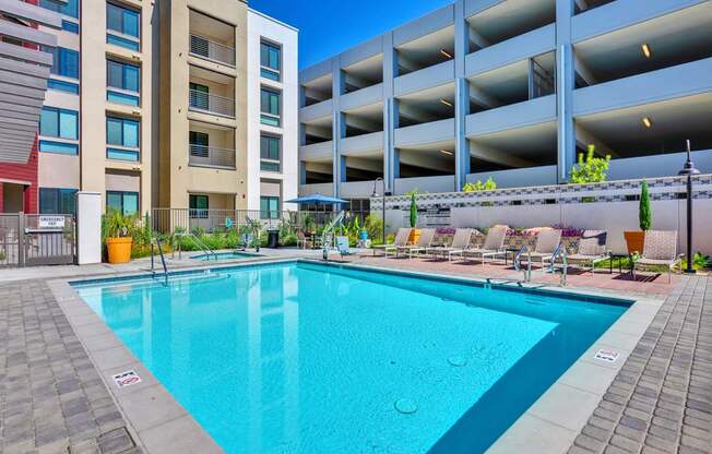A swimming pool surrounded by a brick patio and lounge chairs.