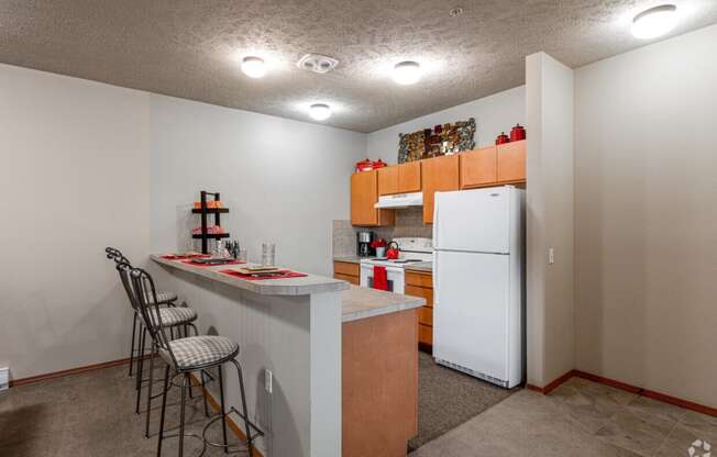 A kitchen with a white refrigerator freezer next to a counter top with three stools