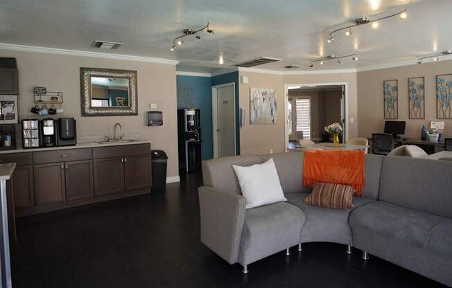 A living room with a grey couch and a kitchen area with a sink and a fridge.