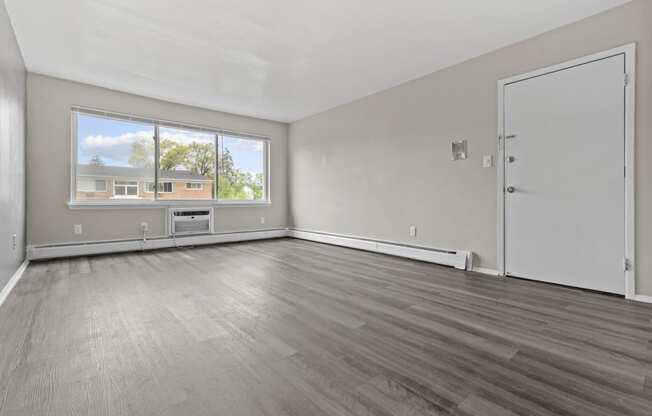 the living room of an empty apartment with wood flooring and a large window