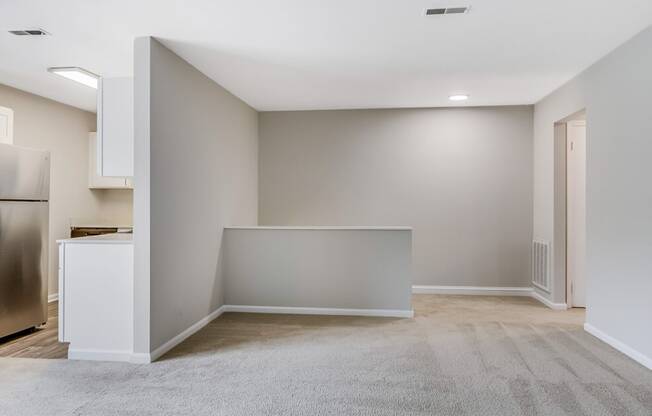 an empty living room with a kitchen and a stainless steel refrigerator