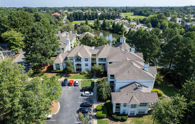 A large white building with a tower is surrounded by trees and has a parking lot in front.