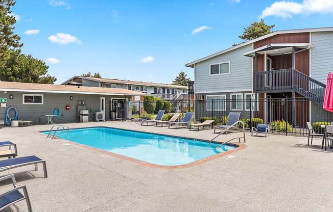 A swimming pool surrounded by lounge chairs and a building in the background t Wildflower Apartments in Kennewick, WA..