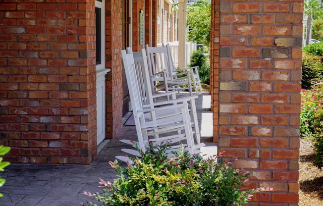 two white rocking chairs on the porch of a brick house